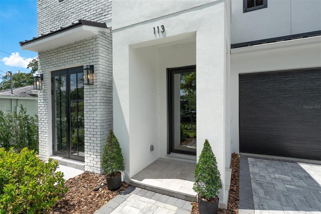 The exterior of a modern home features white stucco, gray brick, and a dark garage door — 113 W EVANS STREET, ORLANDO, FL