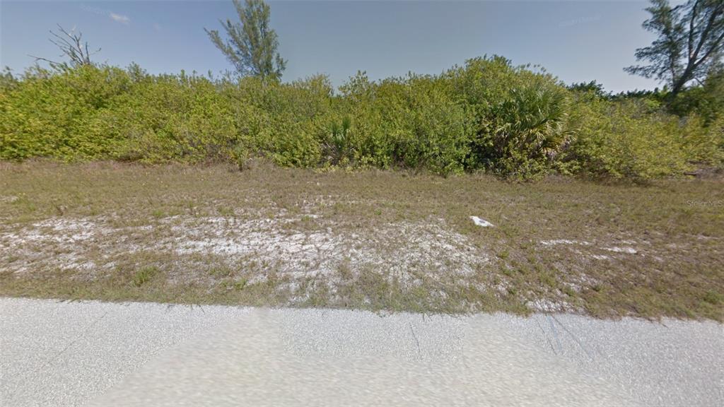 A vacant, grassy lot with sandy soil is bordered by dense green shrubs and trees — 15638 APPLETON BOULEVARD, PORT CHARLOTTE, FL