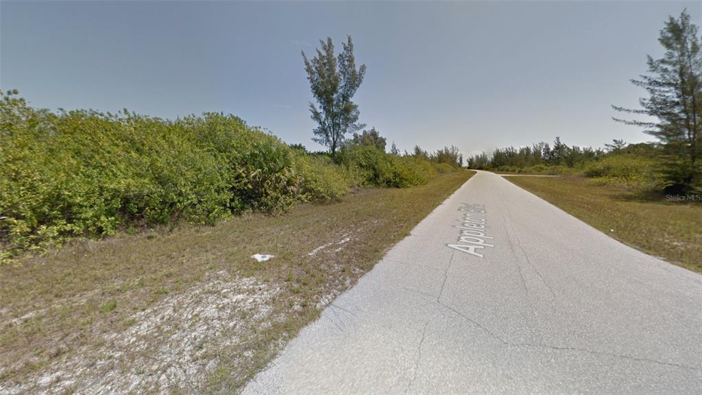 A paved road runs through a vacant, brush-covered lot under a clear sky — 15638 APPLETON BOULEVARD, PORT CHARLOTTE, FL