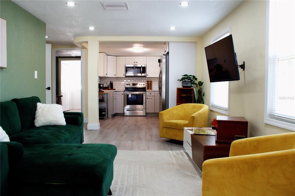 A living room with a green sofa and yellow chairs opens into a white kitchen — 5260 8TH AVENUE N, ST PETERSBURG, FL