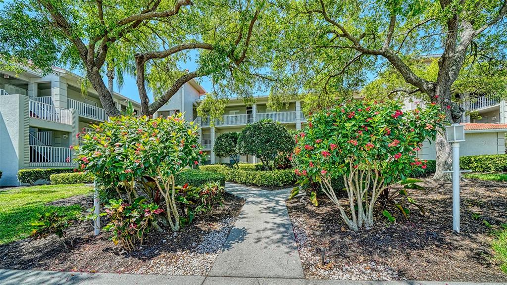 A concrete walkway leads through a landscaped courtyard toward a multi-story apartment building — 9330 CLUBSIDE CIRCLE UNIT 3202, SARASOTA, FL