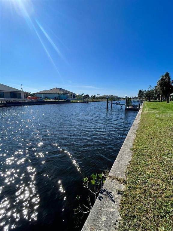 A canal view features a concrete seawall, a small dock, and houses under a clear sky — 15674 MARGO CIRCLE, PORT CHARLOTTE, FL