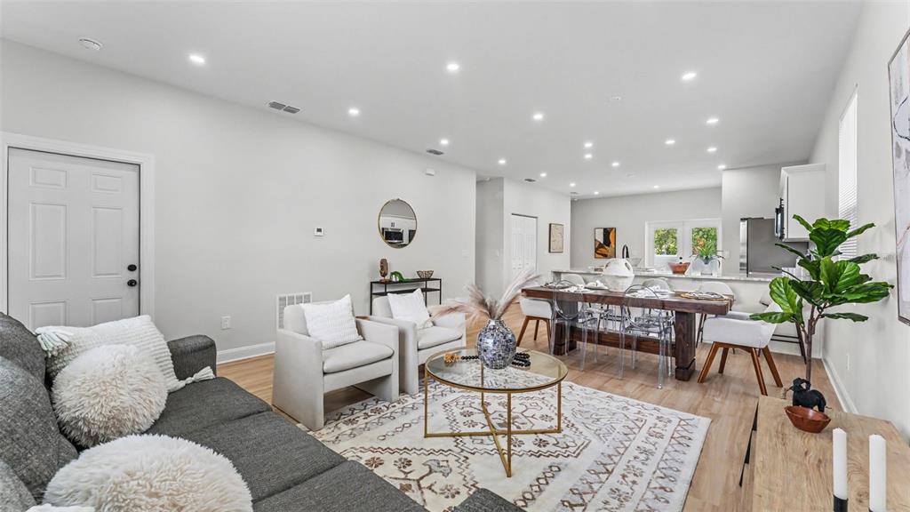 An open-concept living and dining area features light wood flooring, a gray sofa, and chairs — 1305 E PARKER STREET, LAKELAND, FL