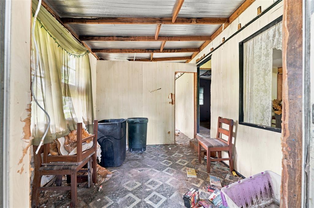 An interior view of a dilapidated sunroom with exposed ceiling rafters, paneled walls, and debris — 13129 CLERMONT STREET, HUDSON, FL