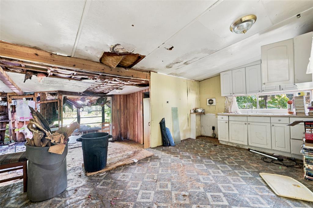 A dilapidated kitchen with damaged ceilings, exposed framing, and white cabinets in a mobile home — 13129 CLERMONT STREET, HUDSON, FL