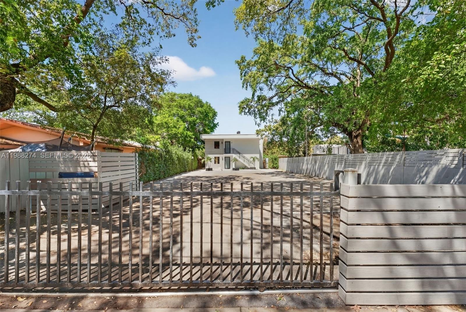 A gated driveway leads to a two-story building surrounded by mature trees and fences — 37 NW 59th St # 4, Miami FL 33127, MIAMI, FL