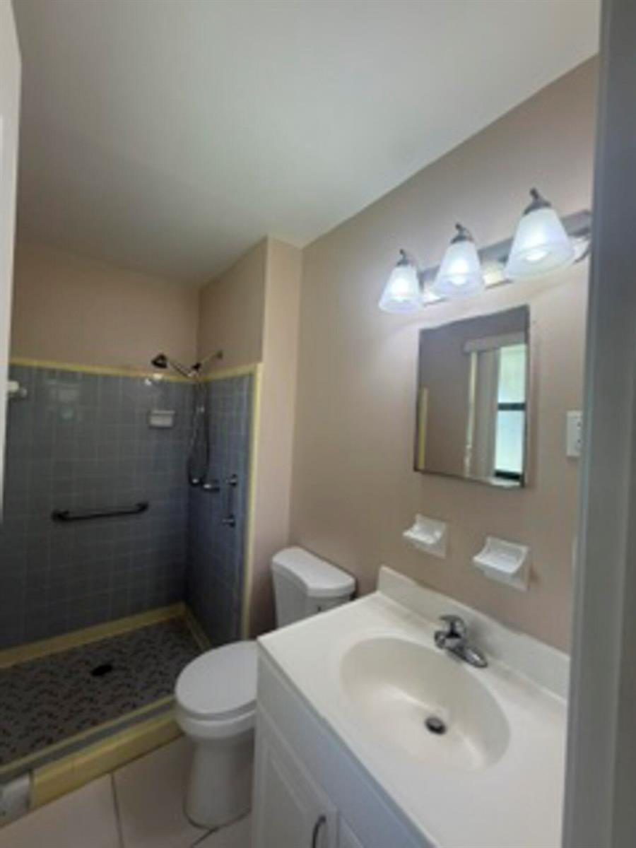 A bathroom features a white vanity, a toilet, and a tiled shower with grab bars — 1102 Greenwood Way, Cocoa FL 32922, COCOA, FL