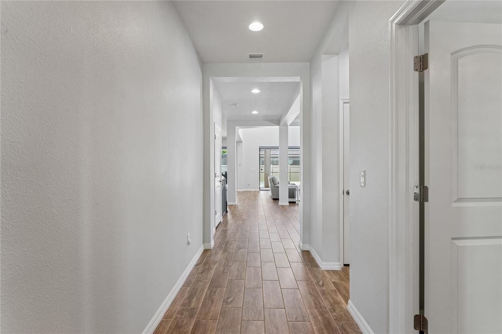 A hallway with light gray walls and wood-look tile flooring leads toward an open living area — 12299 LAKE BLANCHE DRIVE, ODESSA, FL