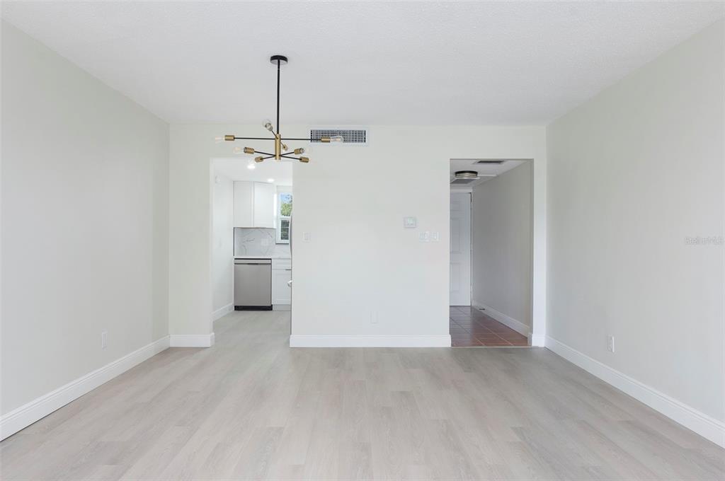 A bright, empty dining room features light wood-look flooring, white walls, and a modern chandelier — 1225 58TH STREET N UNIT 203A, ST PETERSBURG, FL