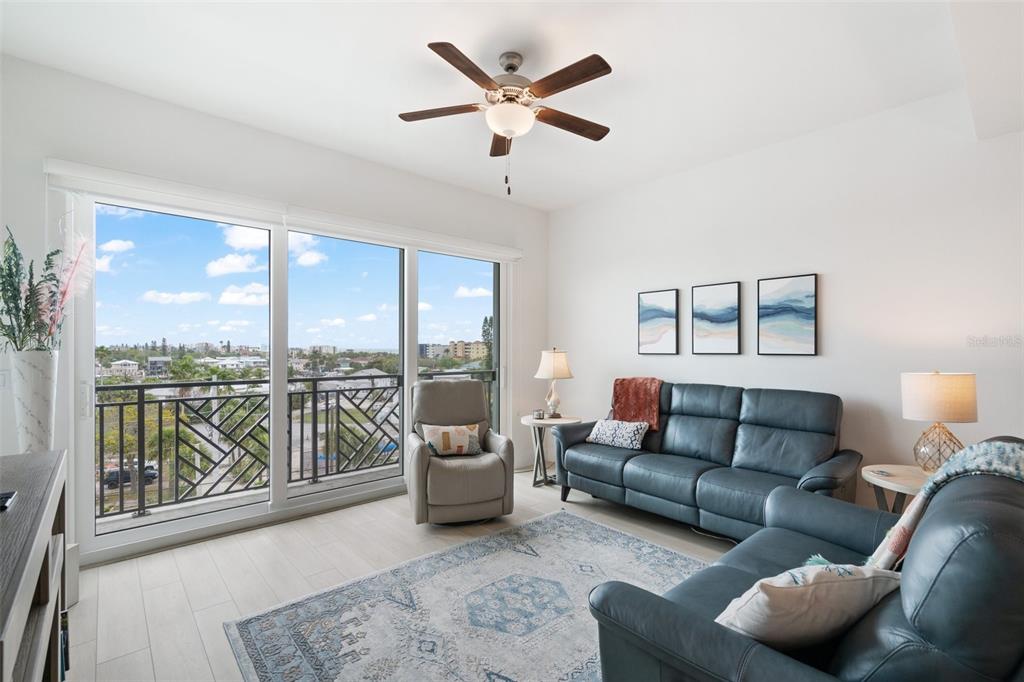 A living room features a blue leather sofa, a recliner, and a balcony with views — 300 150TH AVENUE UNIT 510, MADEIRA BEACH, FL
