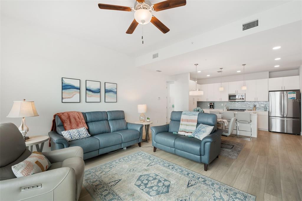 A living room with blue leather sofas, a patterned rug, and an open-concept kitchen — 300 150TH AVENUE UNIT 510, MADEIRA BEACH, FL