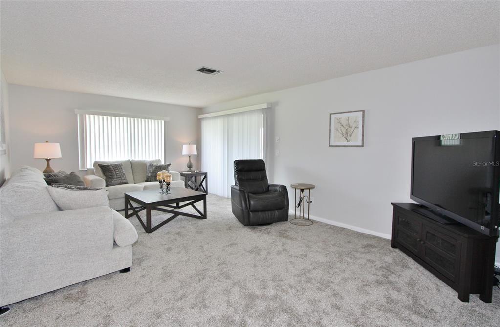 A living room features gray carpet, a light-colored sofa, a dark recliner, and a television — 9635 GREENSKEEPER DRIVE, NEW PORT RICHEY, FL