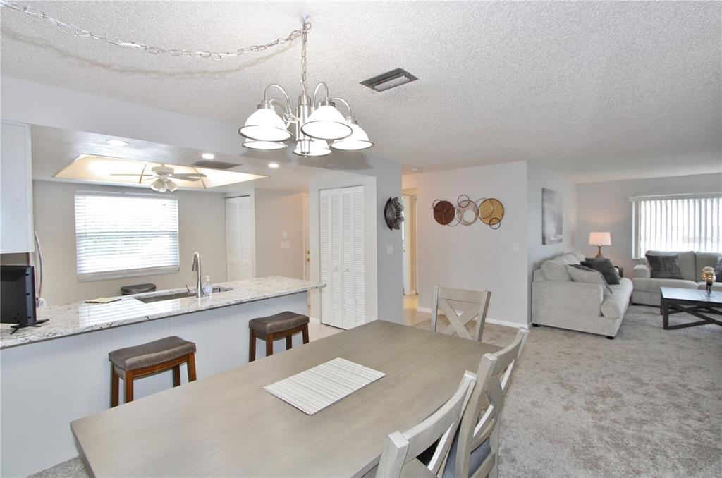 An open-concept dining area with a kitchen island and a living room in the background — 9635 GREENSKEEPER DRIVE, NEW PORT RICHEY, FL