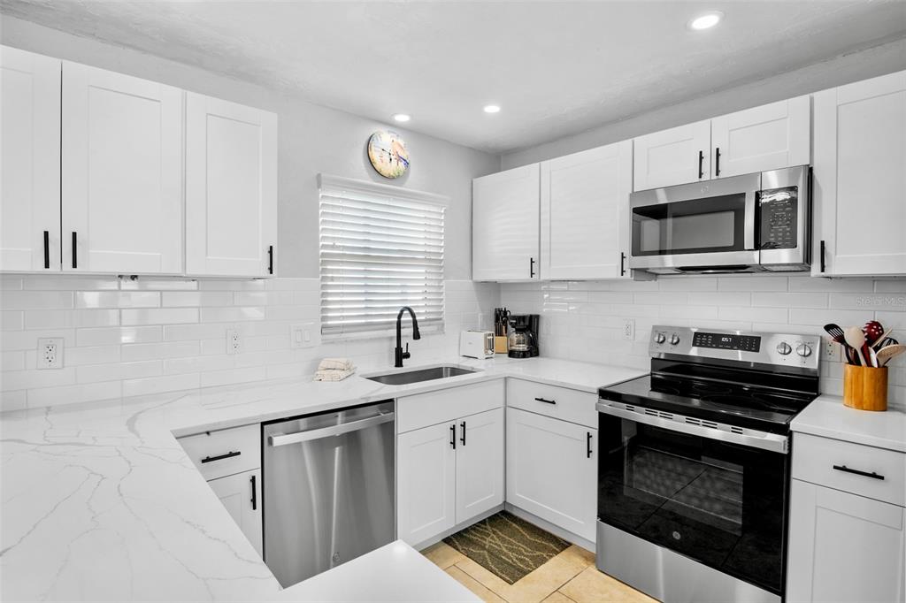 A kitchen features white cabinets, stainless steel appliances, and white countertops with gray veining — 5830 MIDNIGHT PASS ROAD UNIT 93, SARASOTA, FL