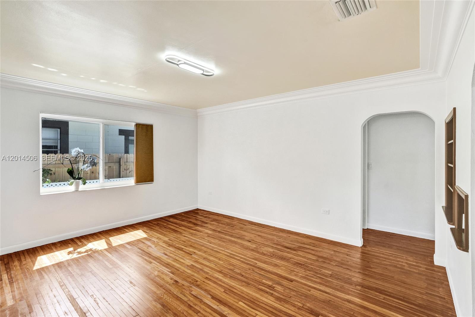 An empty room features white walls, hardwood floors, a window, and an arched doorway — 2420 SW 16th St, Miami FL 33145, MIAMI, FL