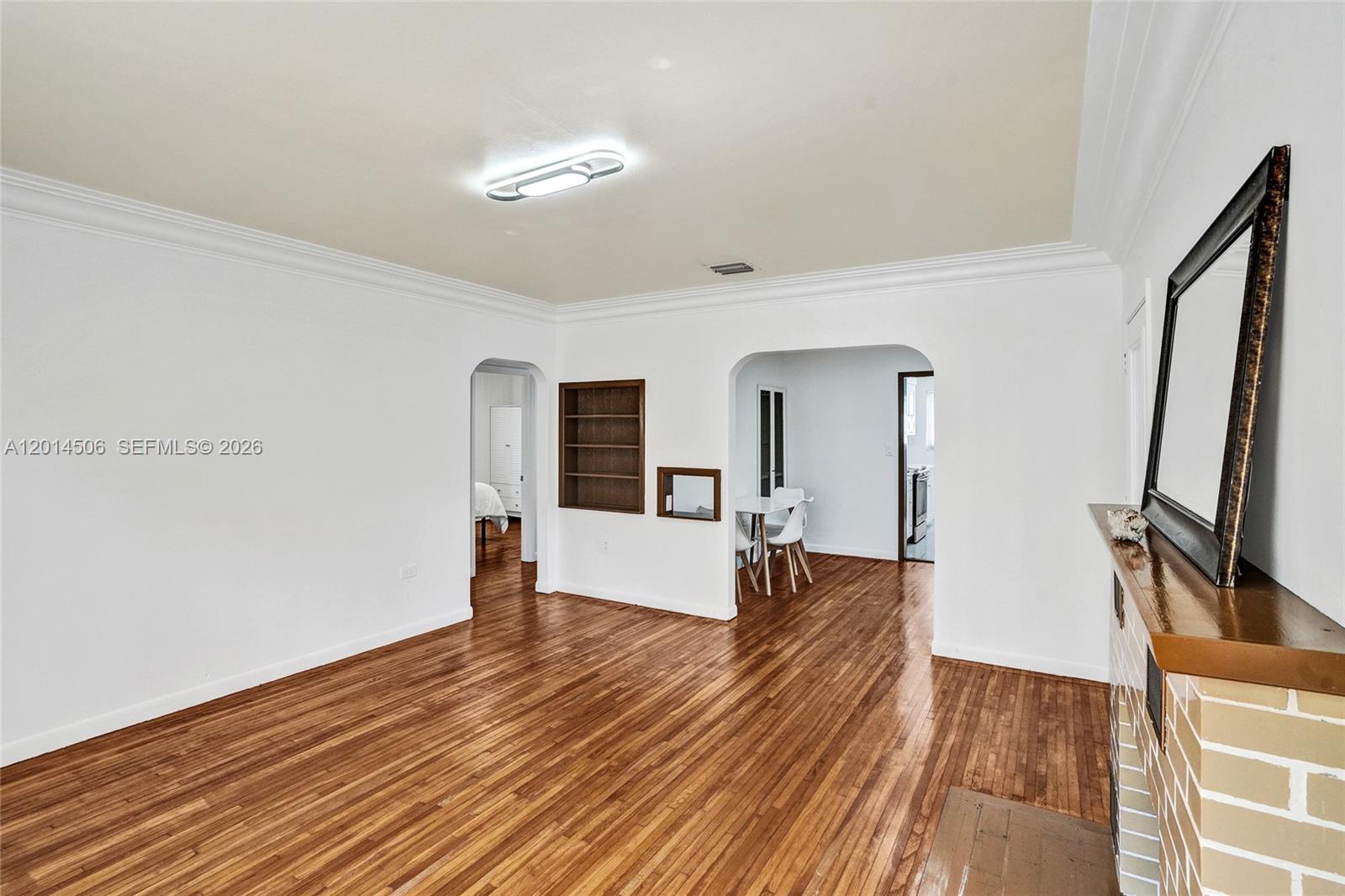 An empty living room features hardwood floors, white walls, arched doorways, and a brick fireplace — 2420 SW 16th St, Miami FL 33145, MIAMI, FL