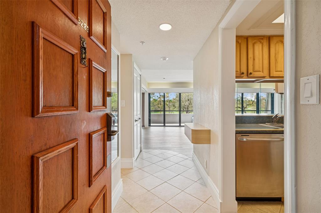 An entryway with a wooden door opens into a tiled hallway leading to a kitchen area — 36750 US 19 N UNIT 22207, PALM HARBOR, FL