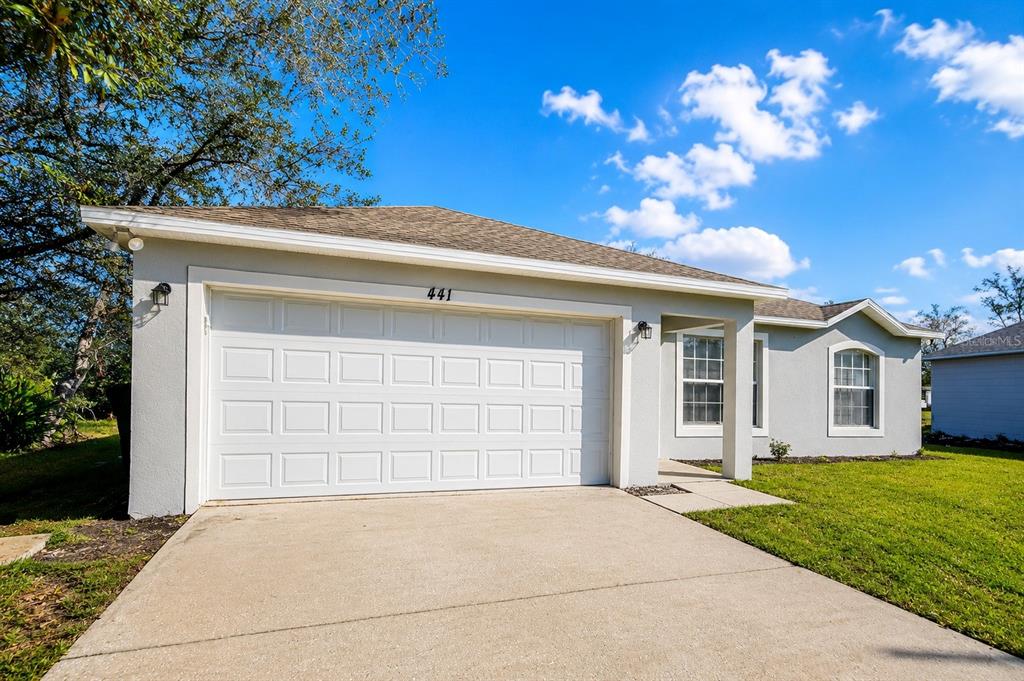 A single-story house exterior features a white garage door, light gray stucco, and a driveway — 441 DANUBE DRIVE, KISSIMMEE, FL