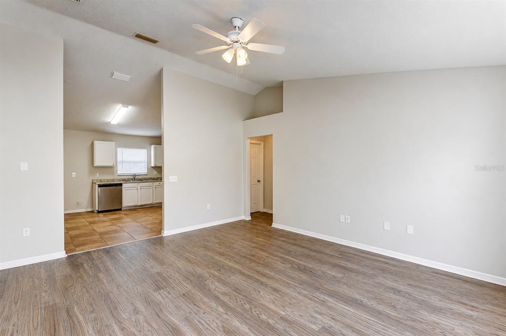 A living room with wood-look flooring and a ceiling fan opens into a tiled kitchen — 441 DANUBE DRIVE, KISSIMMEE, FL