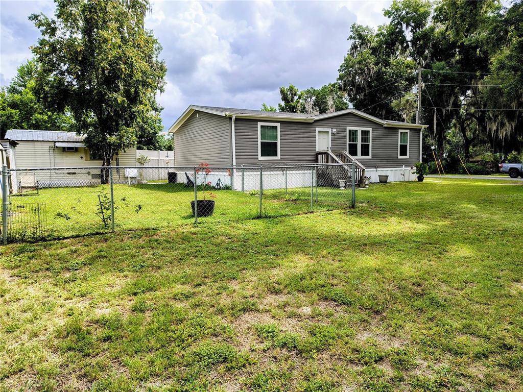 A gray manufactured home with a fenced yard and trees under a cloudy sky — 1912 CR 439C, LAKE PANASOFFKEE, FL