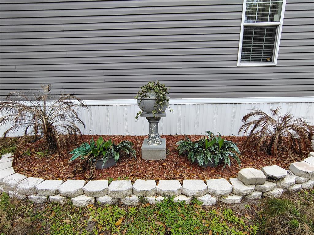 A gray vinyl-sided house exterior features a stone-bordered garden bed with a central pedestal planter — 1912 CR 439C, LAKE PANASOFFKEE, FL