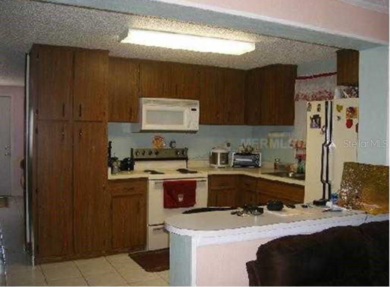 A kitchen features wood cabinets, a white stove, a microwave, and a breakfast bar — 3006 N 44TH STREET, TAMPA, FL