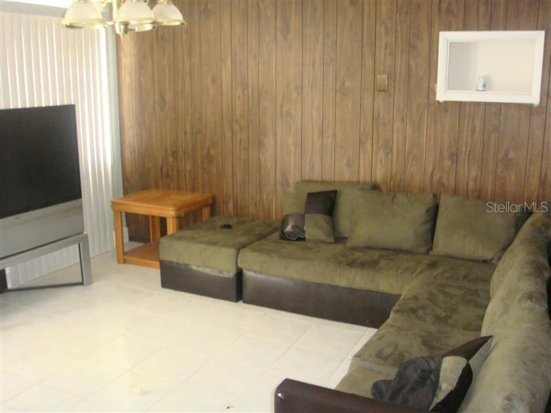 A living room features wood-paneled walls, a large sectional sofa, and a television — 3006 N 44TH STREET, TAMPA, FL