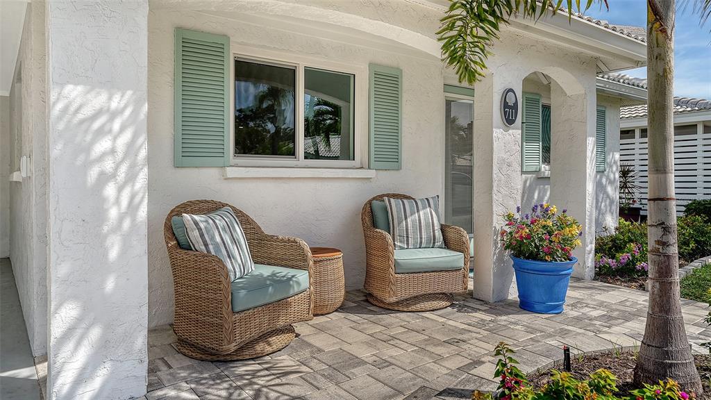 A paved front porch features two wicker chairs with cushions and a blue flower pot — 711 SPANISH DRIVE S, LONGBOAT KEY, FL