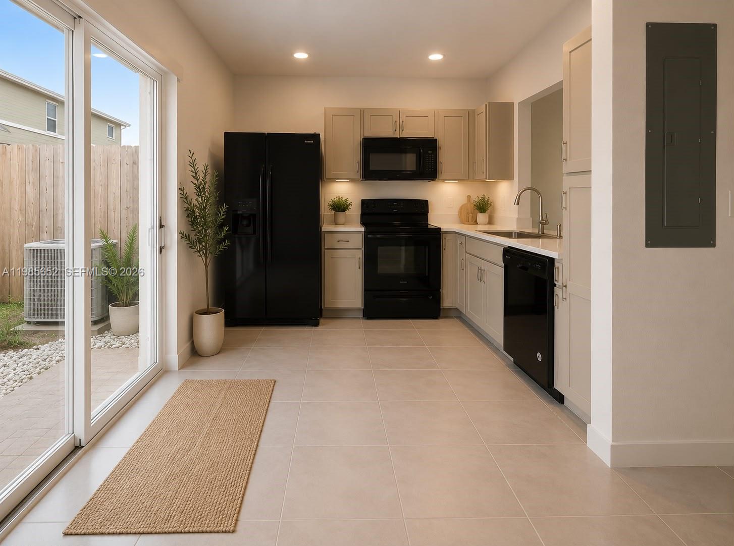 A kitchen features light-colored cabinets, black appliances, tile flooring, and a sliding glass door — 495 NE 5th Ln, Florida City FL 33034, FLORIDA CITY, FL