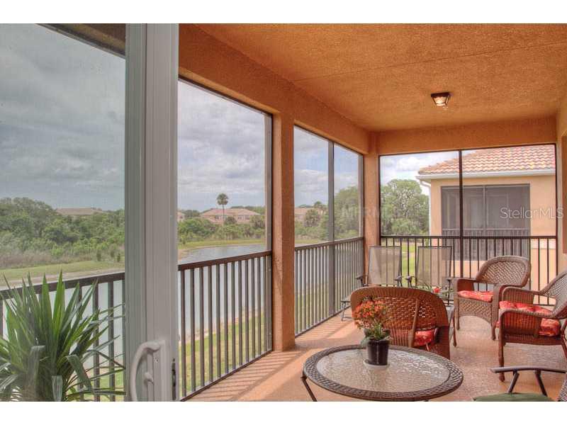 A screened-in balcony with wicker furniture overlooks a lake and neighboring residential buildings — 7312 RIVER HAMMOCK DRIVE UNIT 103, BRADENTON, FL