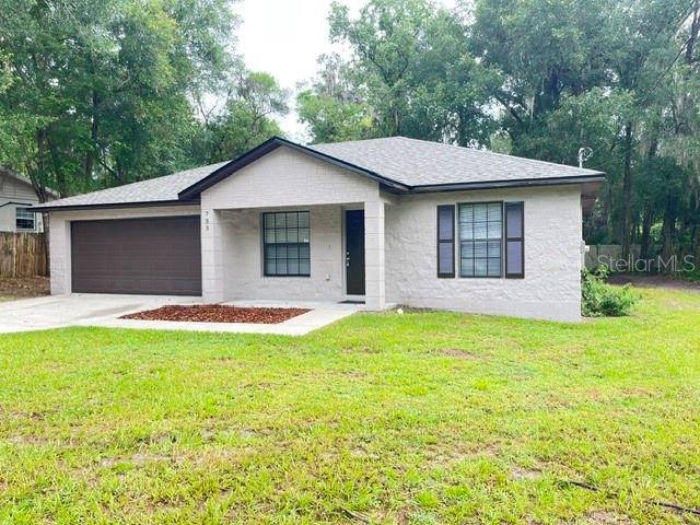 A single-story house with a light-colored brick exterior, a dark roof, and a two-car garage — 733 E INDIANA AVENUE, DELAND, FL