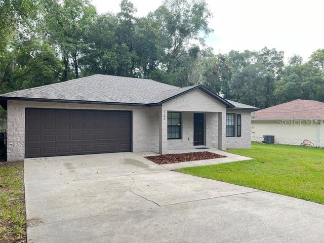 A single-story house with a light-colored brick exterior, a dark garage door, and a driveway — 733 E INDIANA AVENUE, DELAND, FL