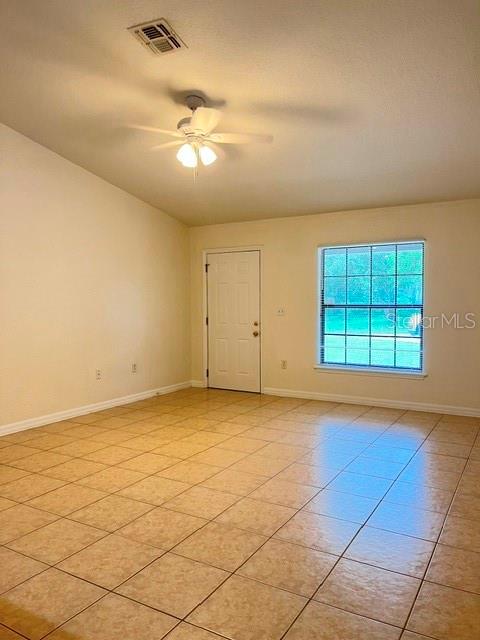 An empty room features beige tile flooring, a ceiling fan, and a white door — 733 E INDIANA AVENUE, DELAND, FL