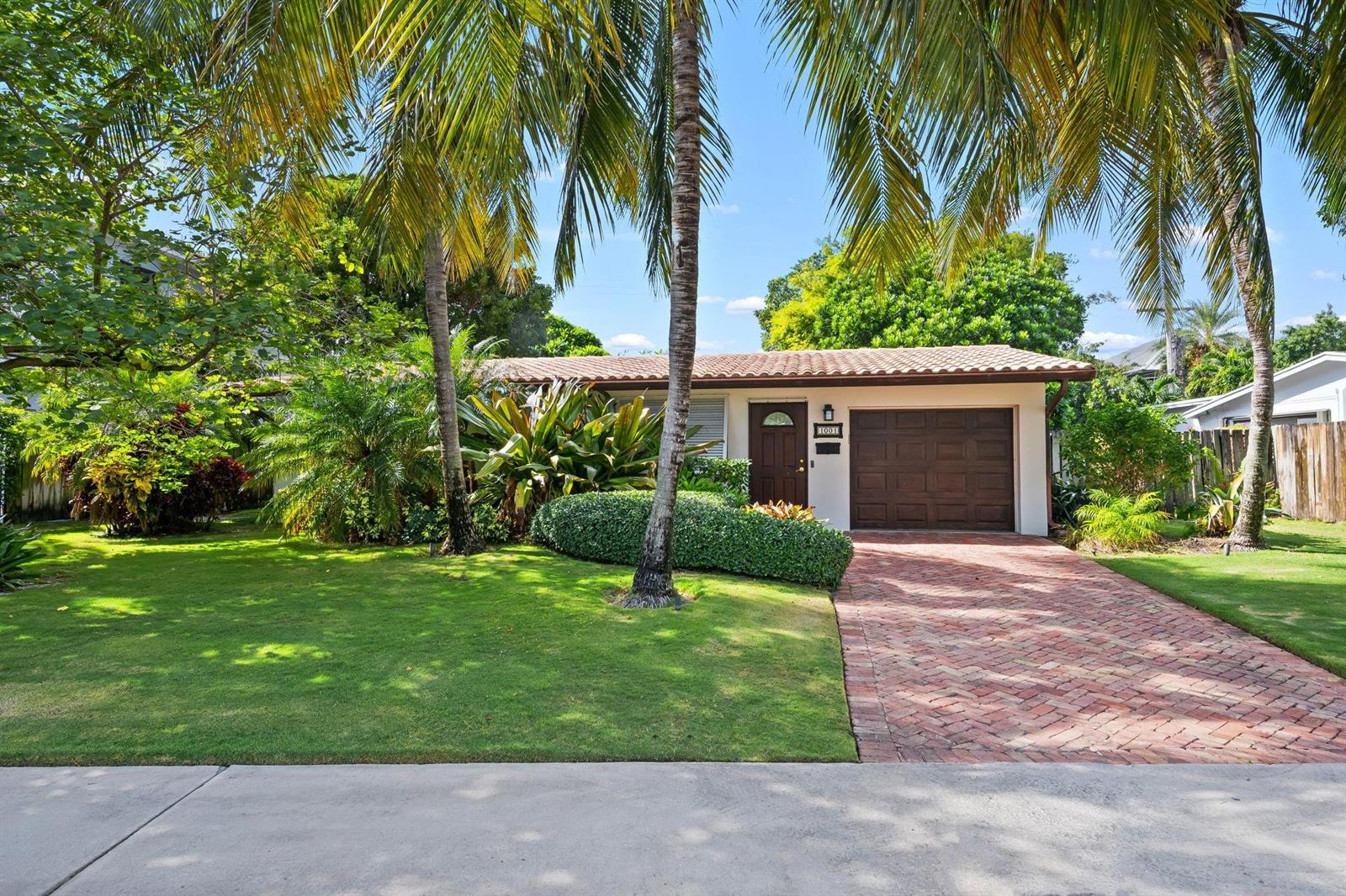 A single-story house with a brick driveway, brown garage door, and palm trees in front — 1001 NE 2nd Terrace, Boca Raton FL 33432, BOCA RATON, FL