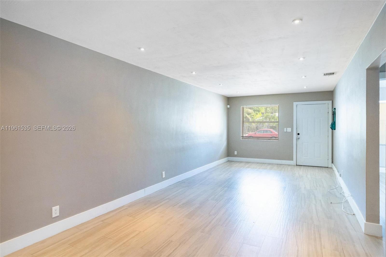 An empty room features light wood-look flooring, gray walls, recessed lighting, and a white door — 551 NE 67th St, Miami FL 33138, MIAMI, FL
