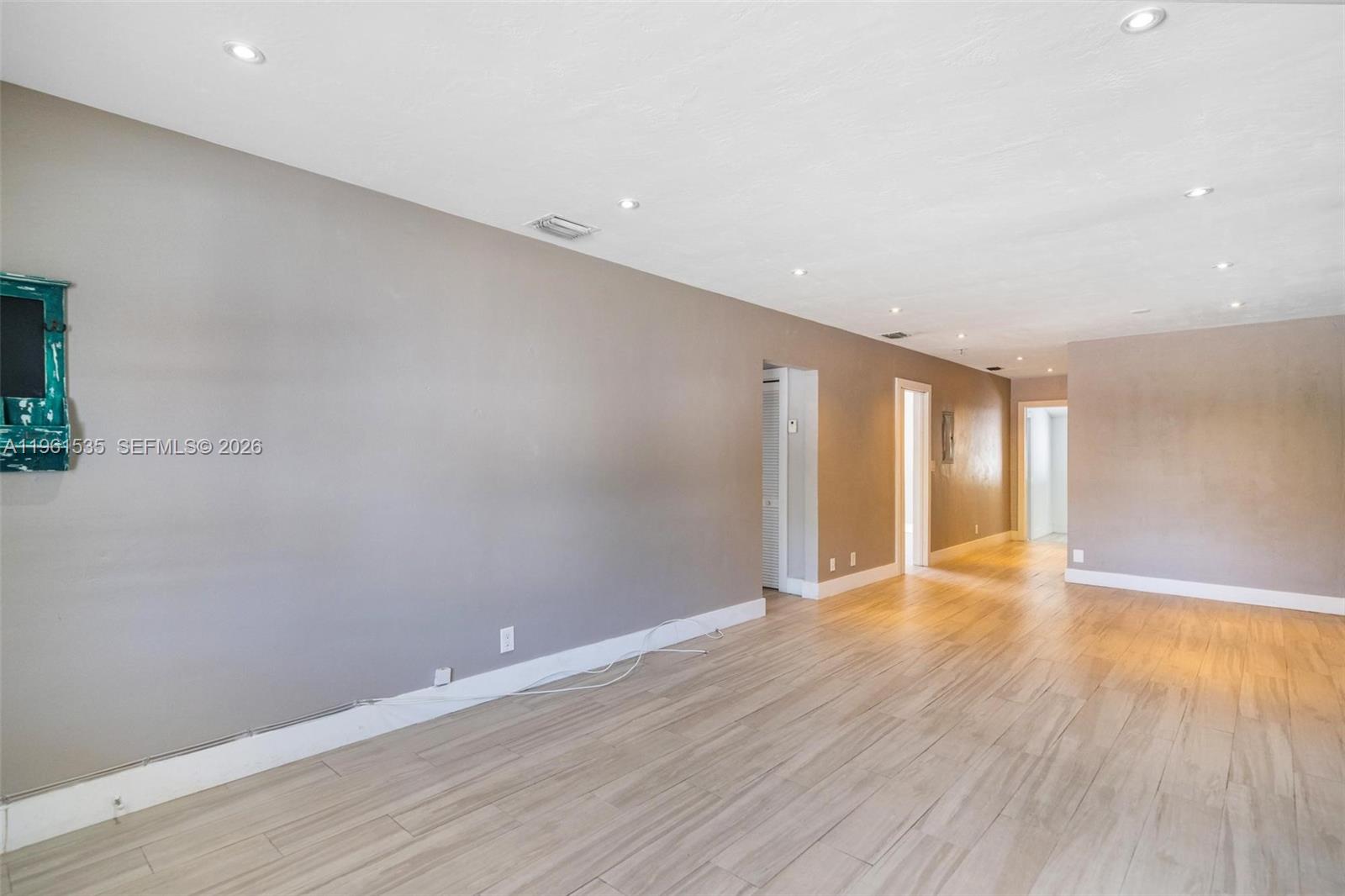 An empty room features light wood-look tile flooring, gray walls, and recessed ceiling lighting — 551 NE 67th St, Miami FL 33138, MIAMI, FL