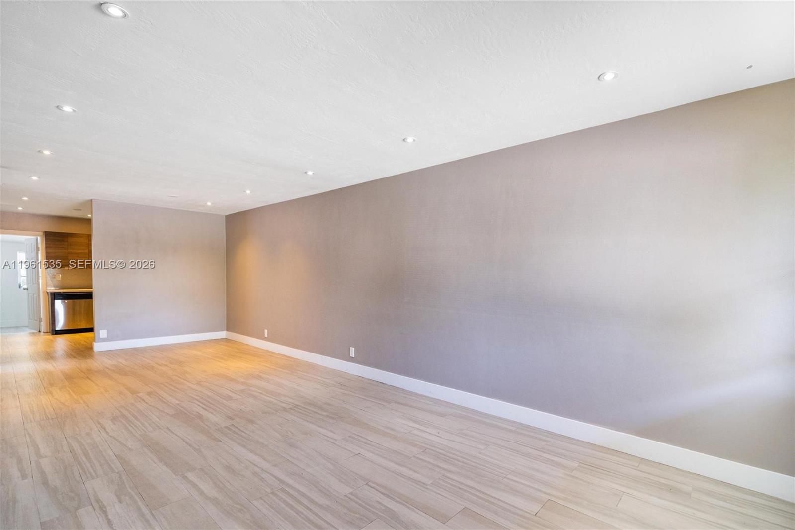 An empty room features light wood-look flooring, recessed ceiling lights, and a large gray wall — 551 NE 67th St, Miami FL 33138, MIAMI, FL