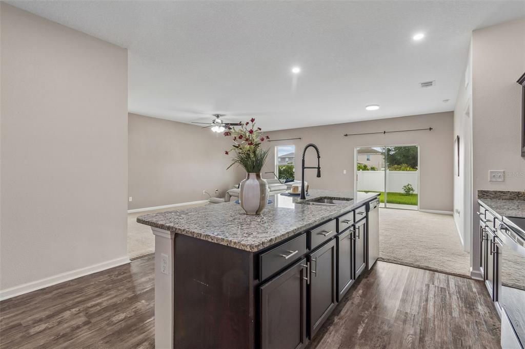 A kitchen island with granite countertops and dark cabinets overlooks a carpeted living area — 1261 ANCHOR BEND DRIVE, RUSKIN, FL
