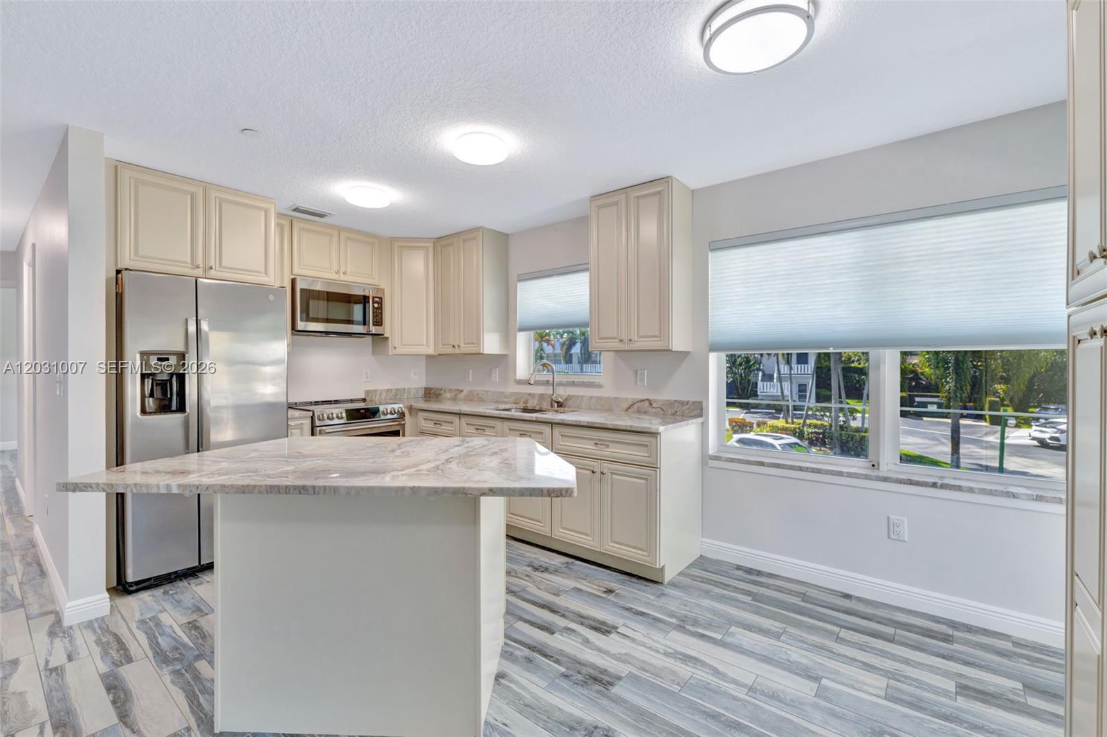 A kitchen features cream-colored cabinets, marble-patterned countertops, stainless steel appliances, and wood-look tile flooring — 2929 SE Ocean Blvd # F6, Stuart FL 34996, STUART, FL