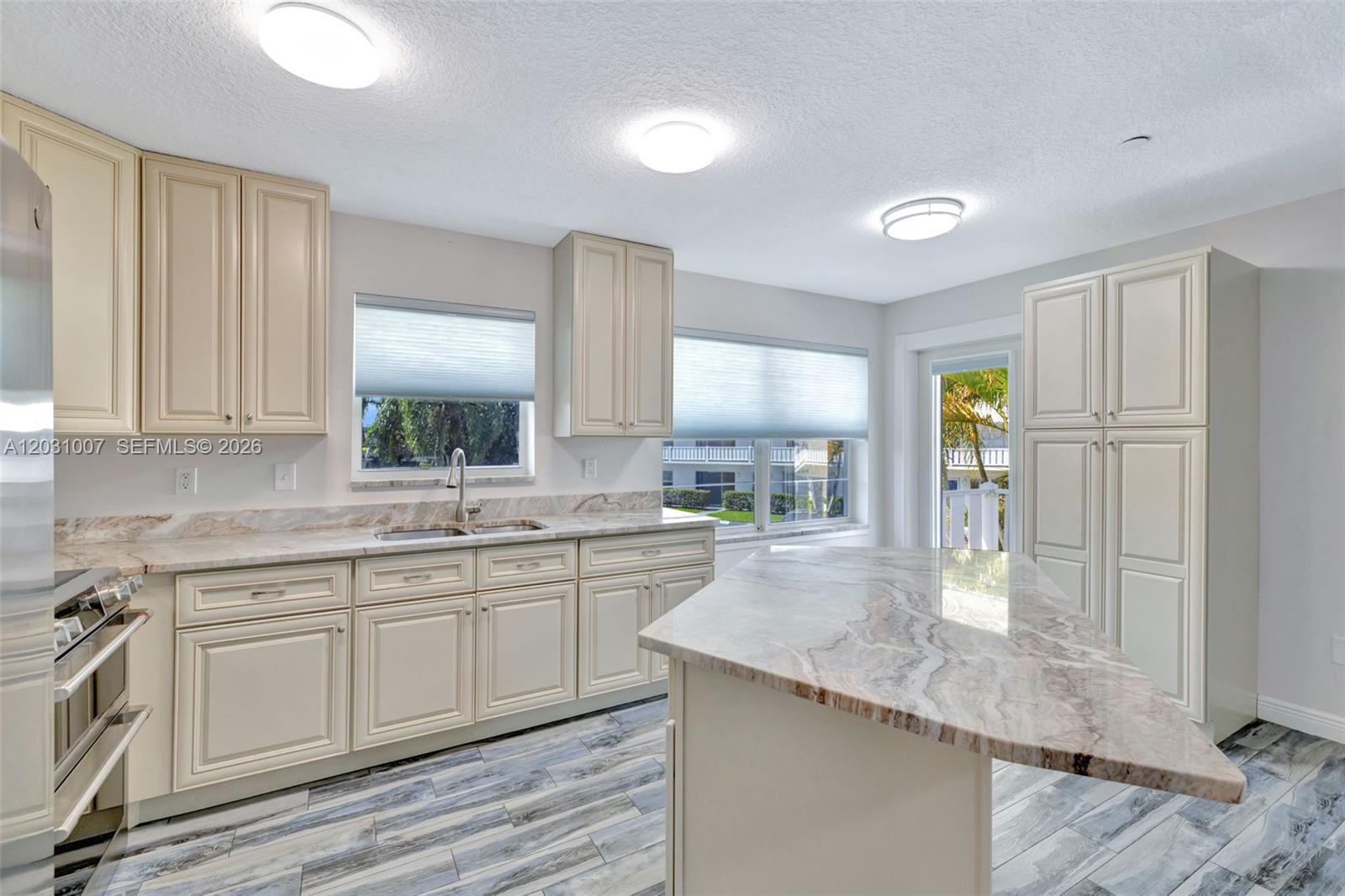 A kitchen features cream-colored cabinetry, marble-patterned countertops, an island, and wood-look tile flooring — 2929 SE Ocean Blvd # F6, Stuart FL 34996, STUART, FL