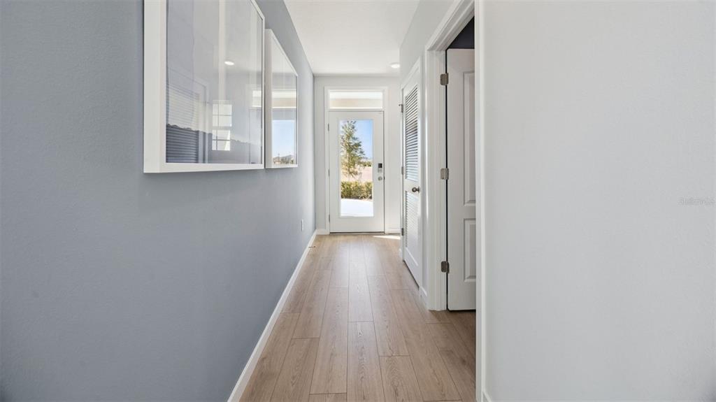 A hallway with light wood flooring, blue walls, framed art, and a glass-paneled exterior door — 1334 CAMELLIA BLOOM LANE, SANFORD, FL