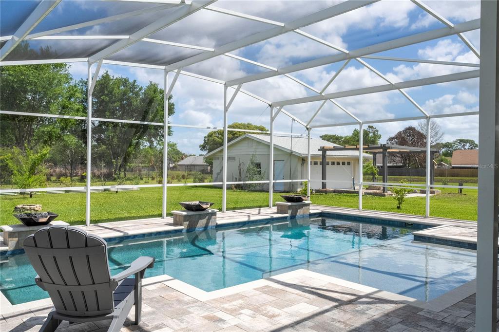 A screened-in patio features a rectangular swimming pool with stone fire bowls on the deck — 8595 MILLINOCKETT LANE, ORLANDO, FL