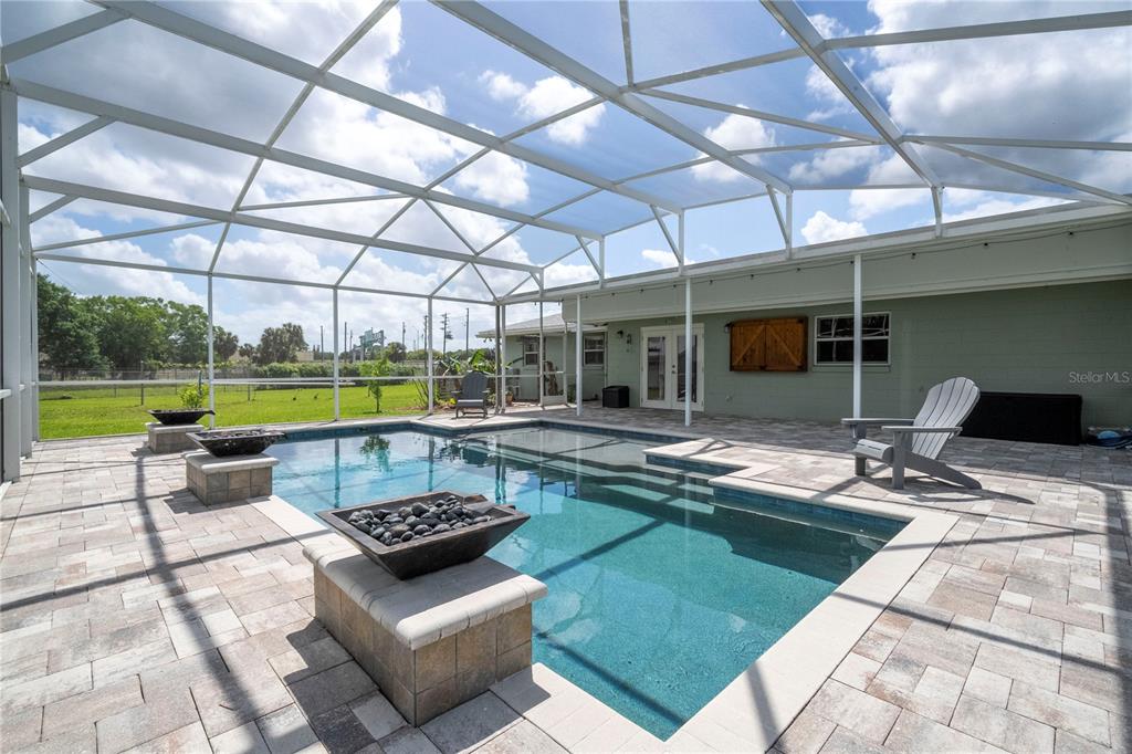 A screened-in patio features a rectangular swimming pool with fire bowls and paver decking — 8595 MILLINOCKETT LANE, ORLANDO, FL