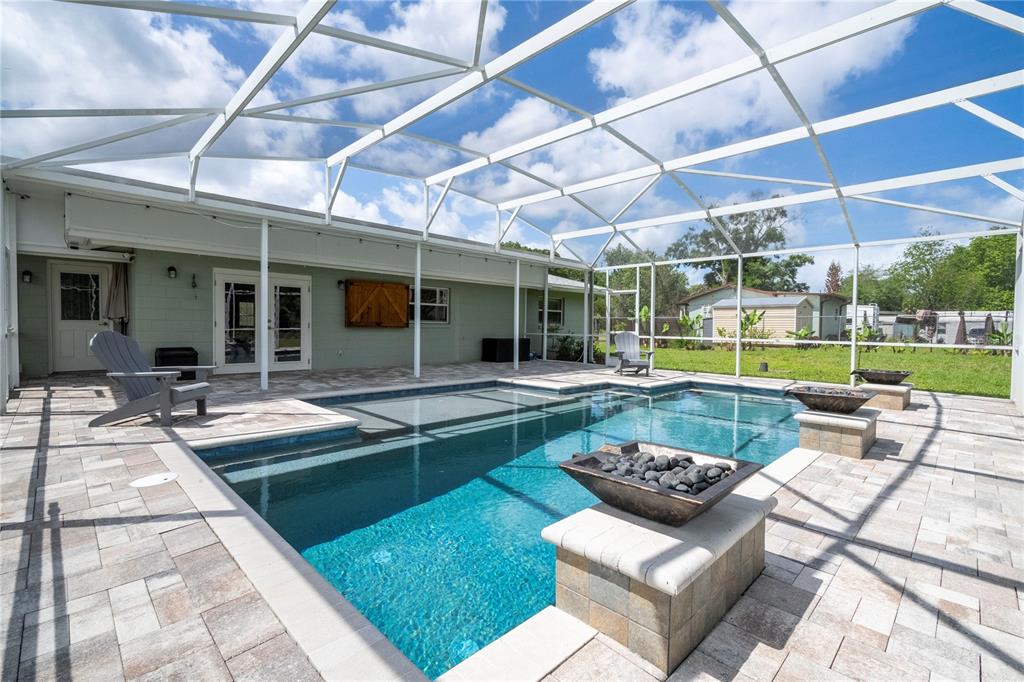 A screened-in patio features a rectangular swimming pool with two fire bowls on pedestals — 8595 MILLINOCKETT LANE, ORLANDO, FL