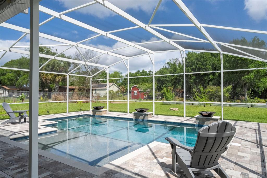 A screened-in swimming pool with stone fire bowls on a paved patio overlooking a yard — 8595 MILLINOCKETT LANE, ORLANDO, FL