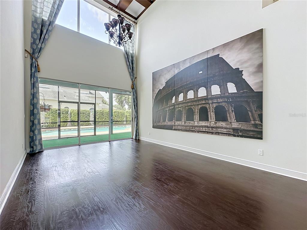 A high-ceilinged room with dark wood floors, a large Colosseum wall mural, and pool views — 2705 KNIGHTSBRIDGE ROAD, CLERMONT, FL