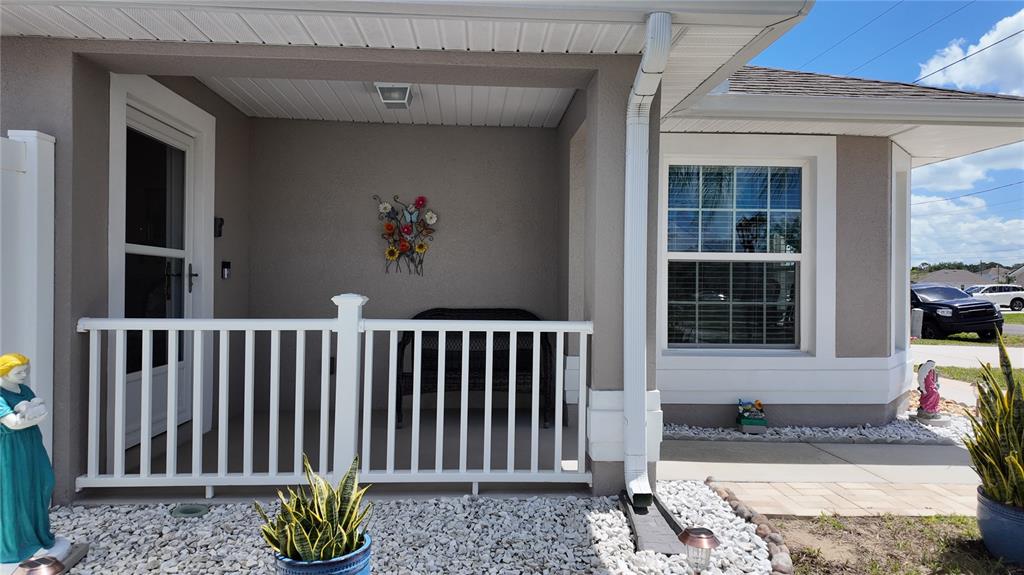 A covered front porch features a white railing, a bench, and a decorative wall hanging — 1220 N PLATTE COURT E, POINCIANA, FL