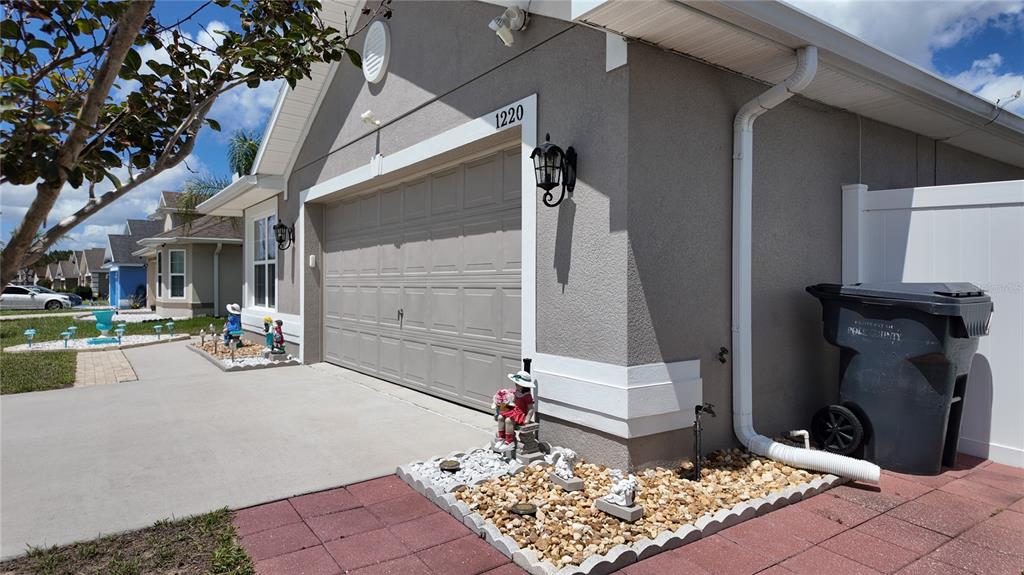 The exterior of a house features a garage, a gravel garden bed, and a trash bin — 1220 N PLATTE COURT E, POINCIANA, FL