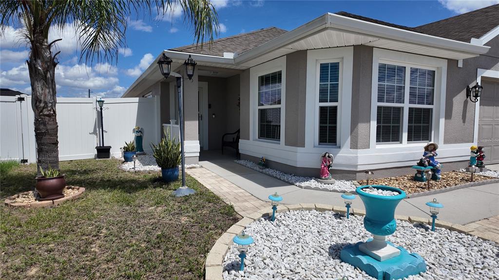 A single-story house exterior features a paved walkway, white vinyl fencing, and decorative garden statues — 1220 N PLATTE COURT E, POINCIANA, FL