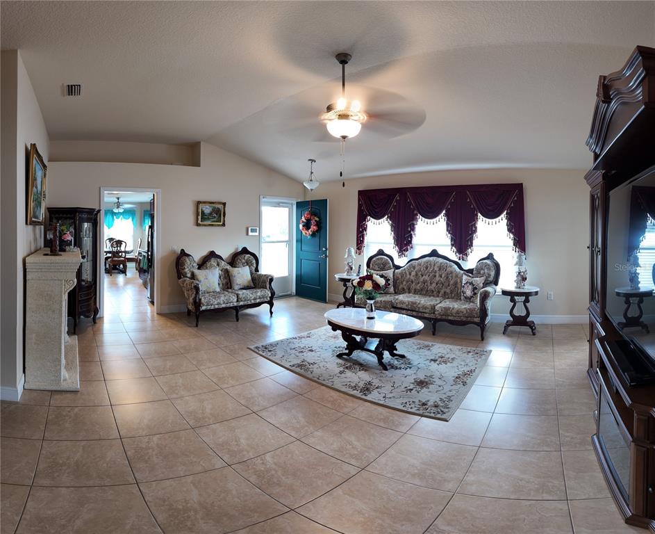 A living room with tile floors, a ceiling fan, ornate furniture, and a large window — 1220 N PLATTE COURT E, POINCIANA, FL